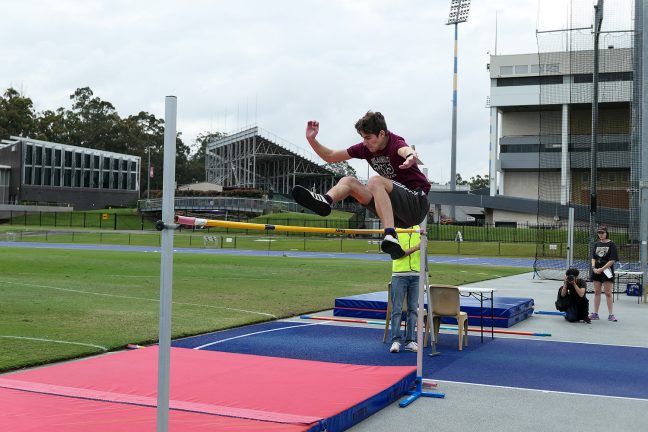 Male athlete jumping over a high jump at Faith Christian School's athletics carnival day at QSAC